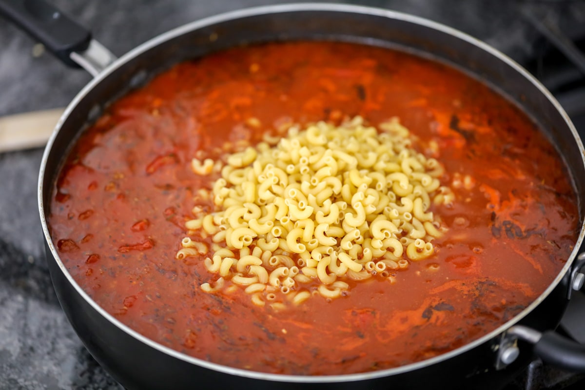 Adding macaroni pasta to a skillet on the stove.