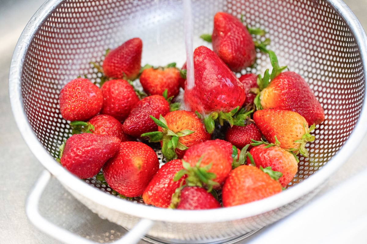 Strawberries being rinsed in colander.