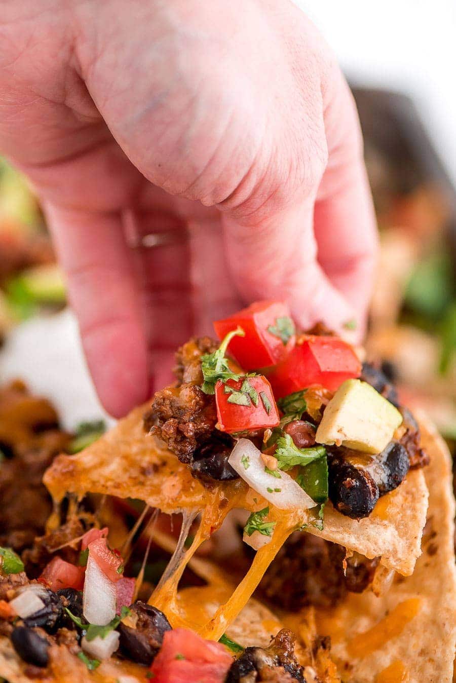Pulling a chunk of Loaded Nachos Recipe covered with toppings.