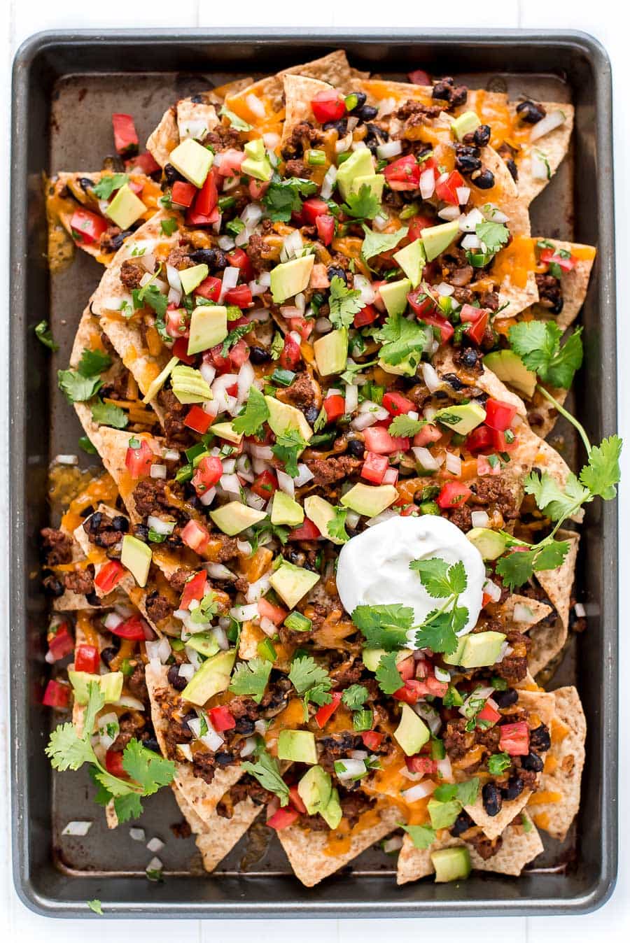 Loaded Nachos topped with sour cream and cilantro served on sheet pan.