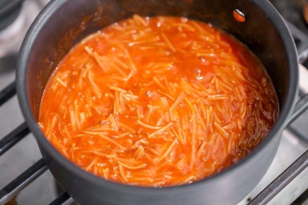 Adding sauce to pasta in a pot on the stove.