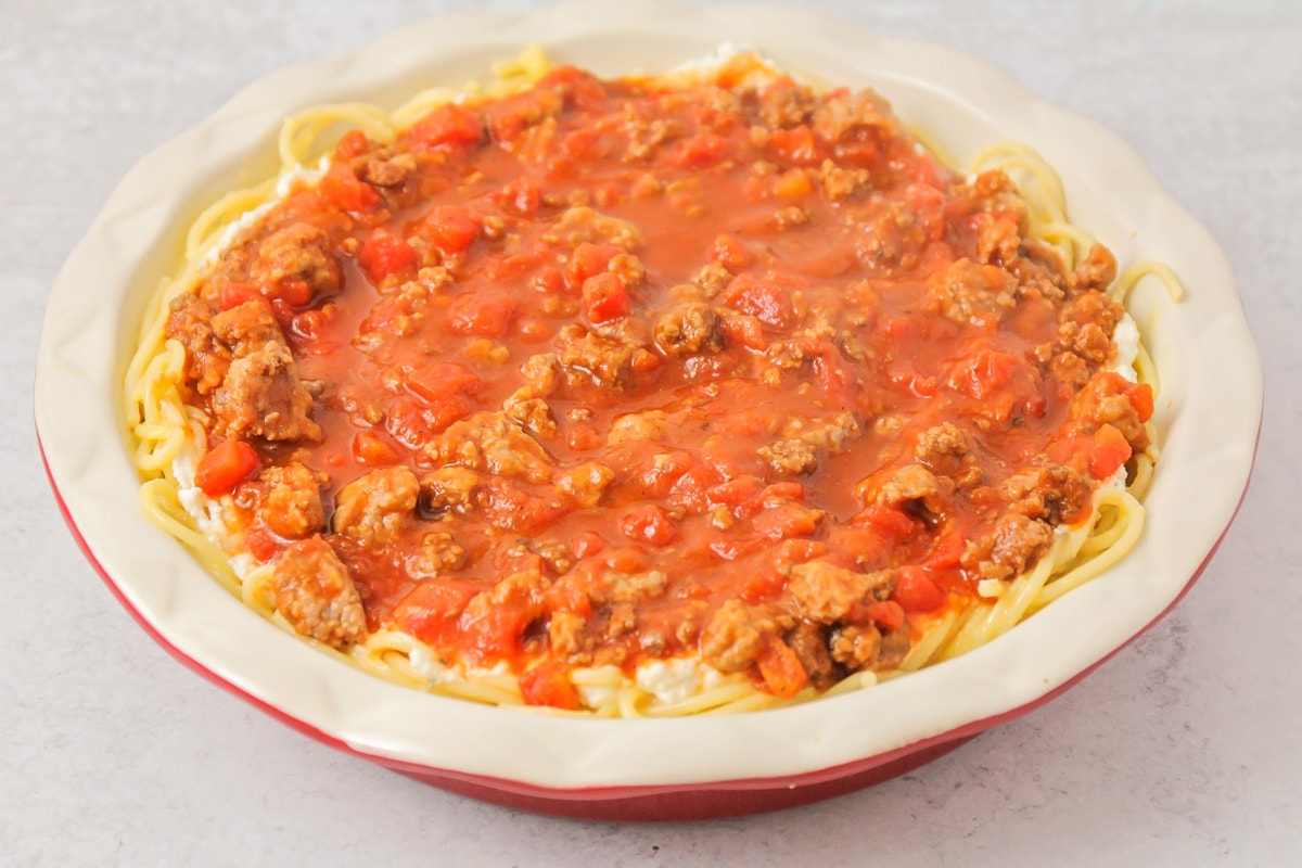 Noodle, cheese, meat and sauce in pie dish.