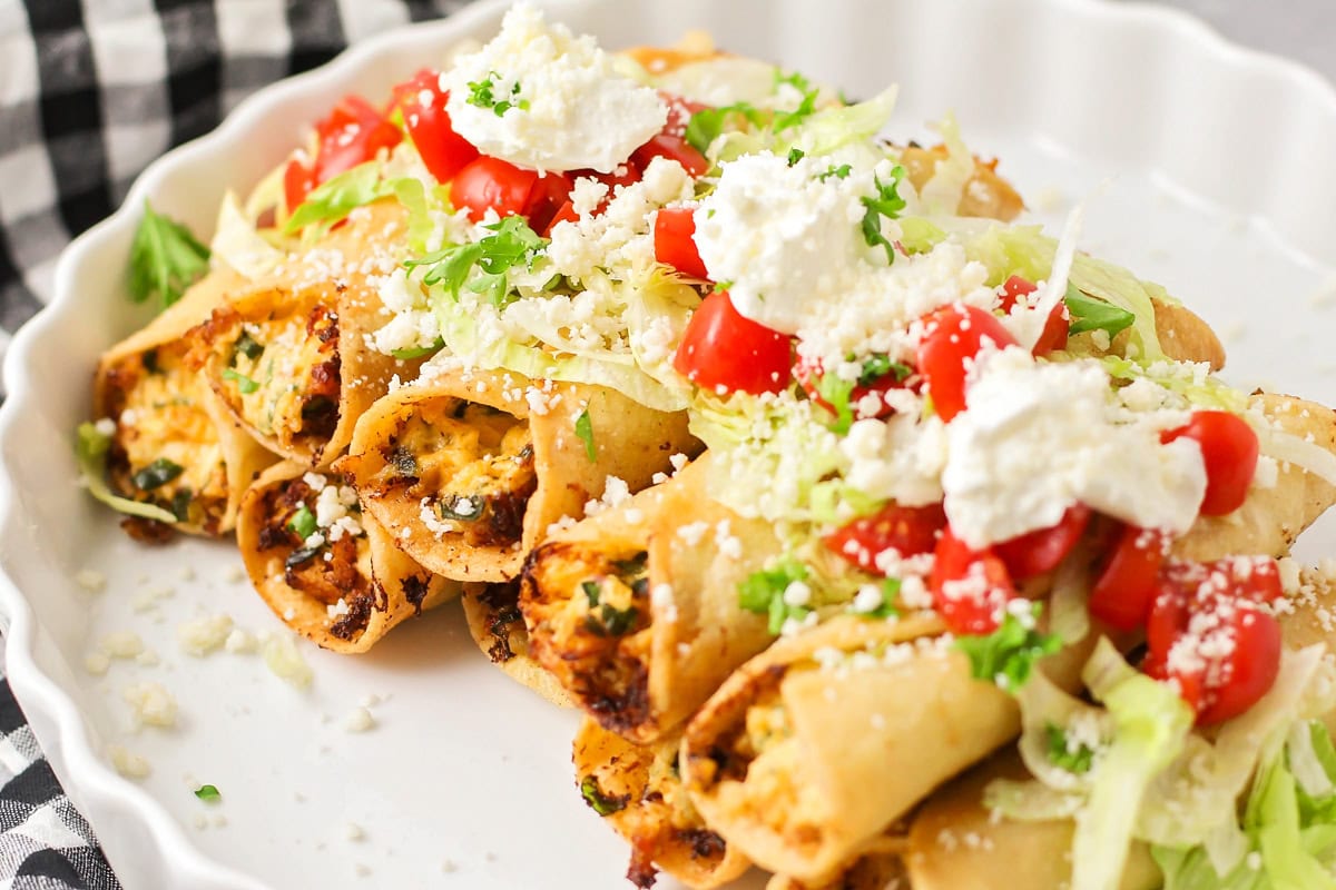 Taquitos stacked on top of each other and topped with lettuce, tomatoes, cheese and more.