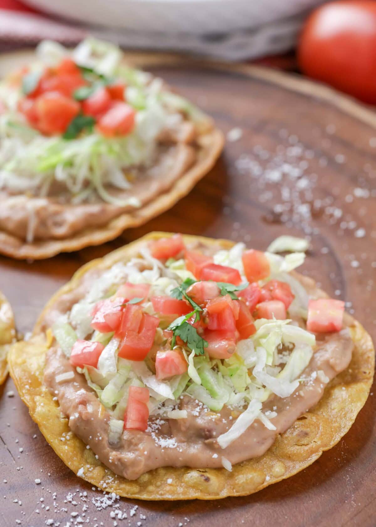 Easy tostada recipe with beans, lettuce, tomatoes and more on top.