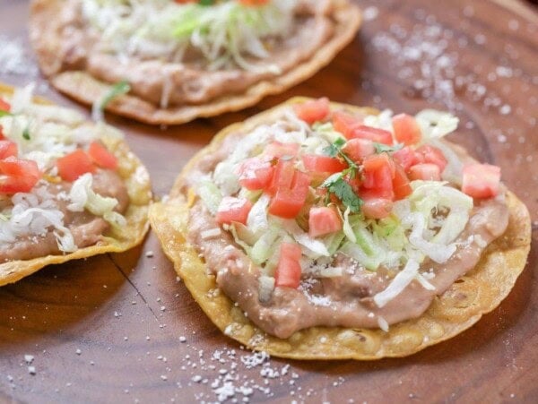 Three tostadas topped with refried beans, lettuce, tomatoes, and cilantro.