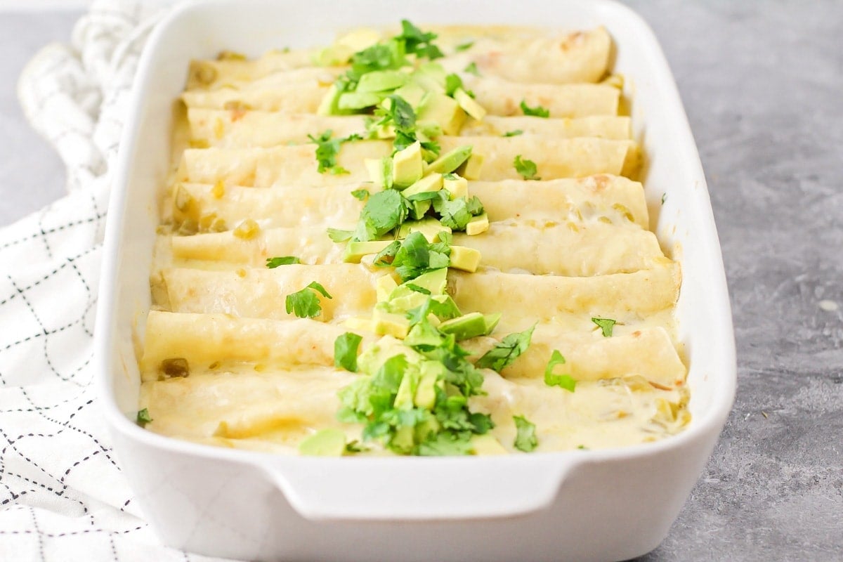 A baking dish filled with white chicken enchiladas topped with cilantro and avocado.