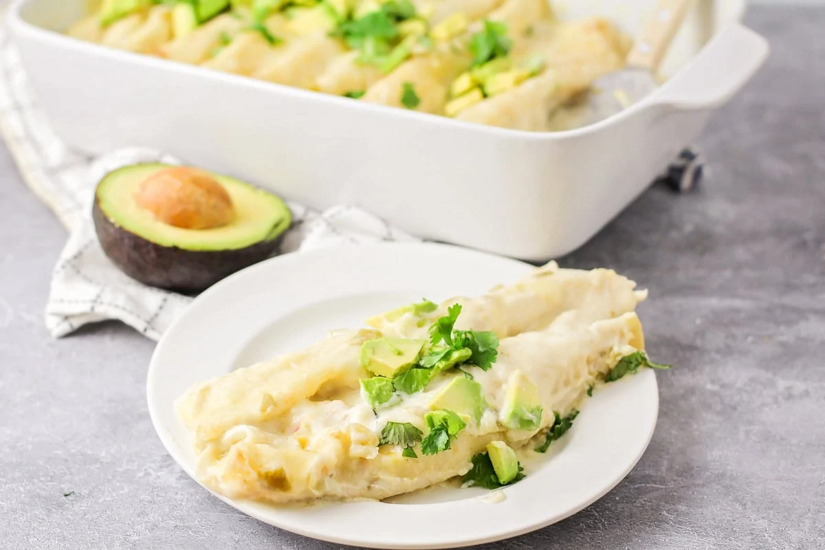 Two white chicken enchiladas on white plate.