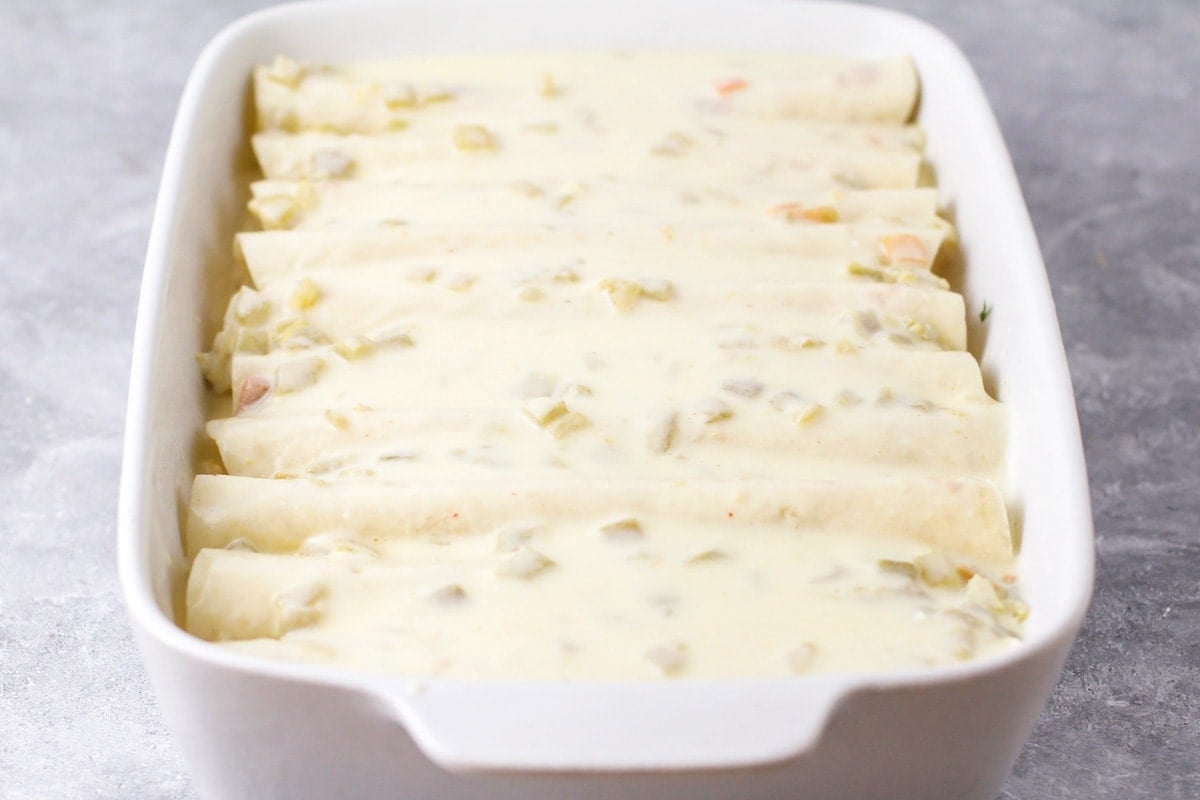 Rolled enchiladas topped with white green chile sauce.