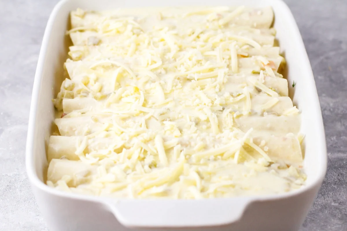 Cheese poured on top of white chicken enchiladas.
