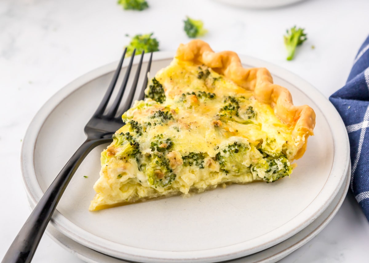 A slice of broccoli quiche served on a white plate.