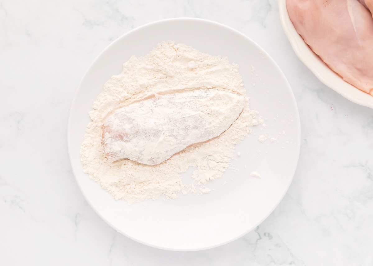 Dredging chicken breast in a bowl of flour.