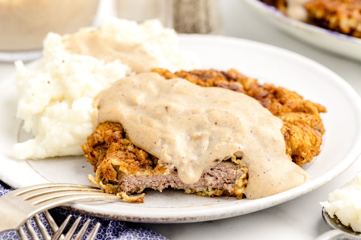 Country gravy recipe poured over country fried steak and mashed potatoes.