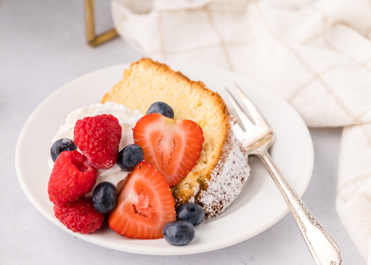 A slice of pound cake served with fresh fruit and whipped cream.