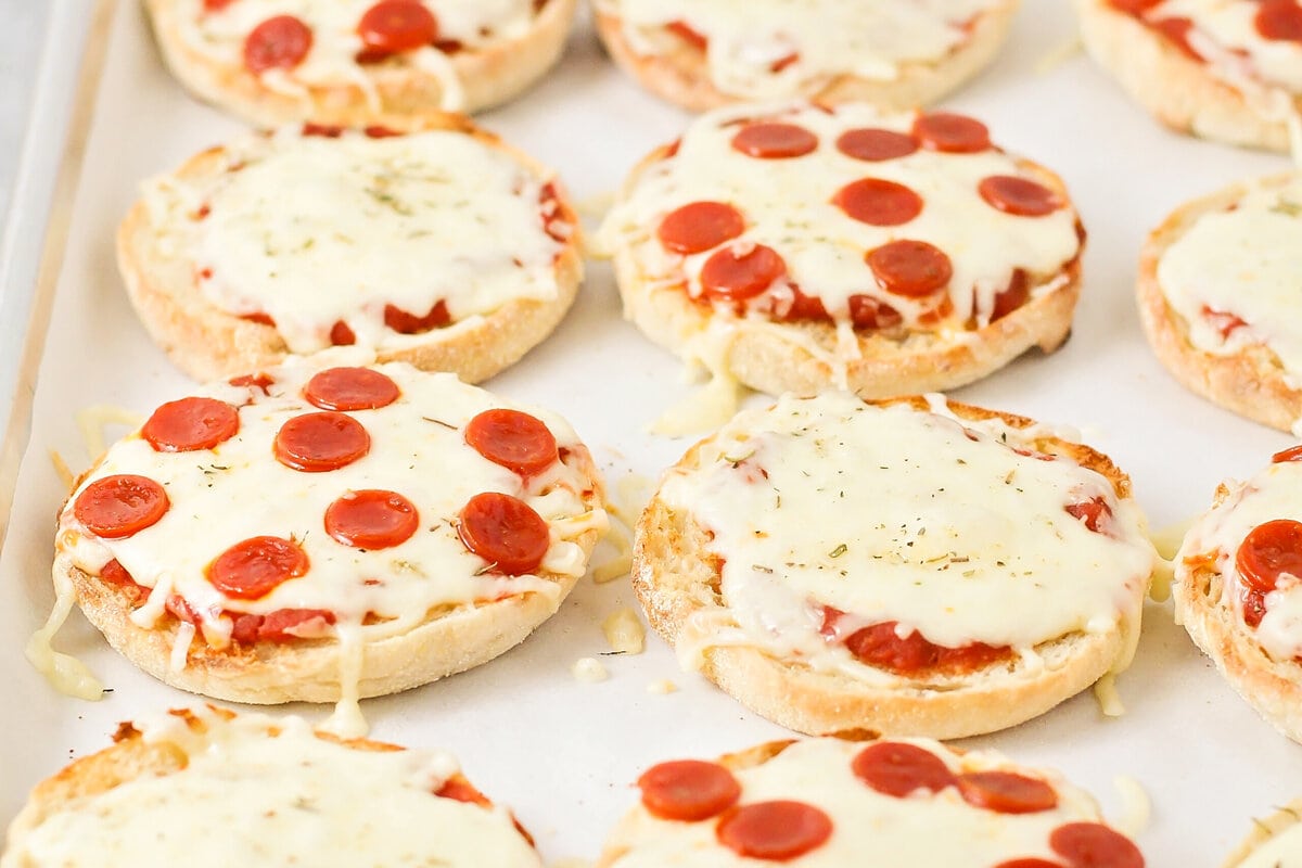 Several english muffin pizzas on a lined baking sheet.