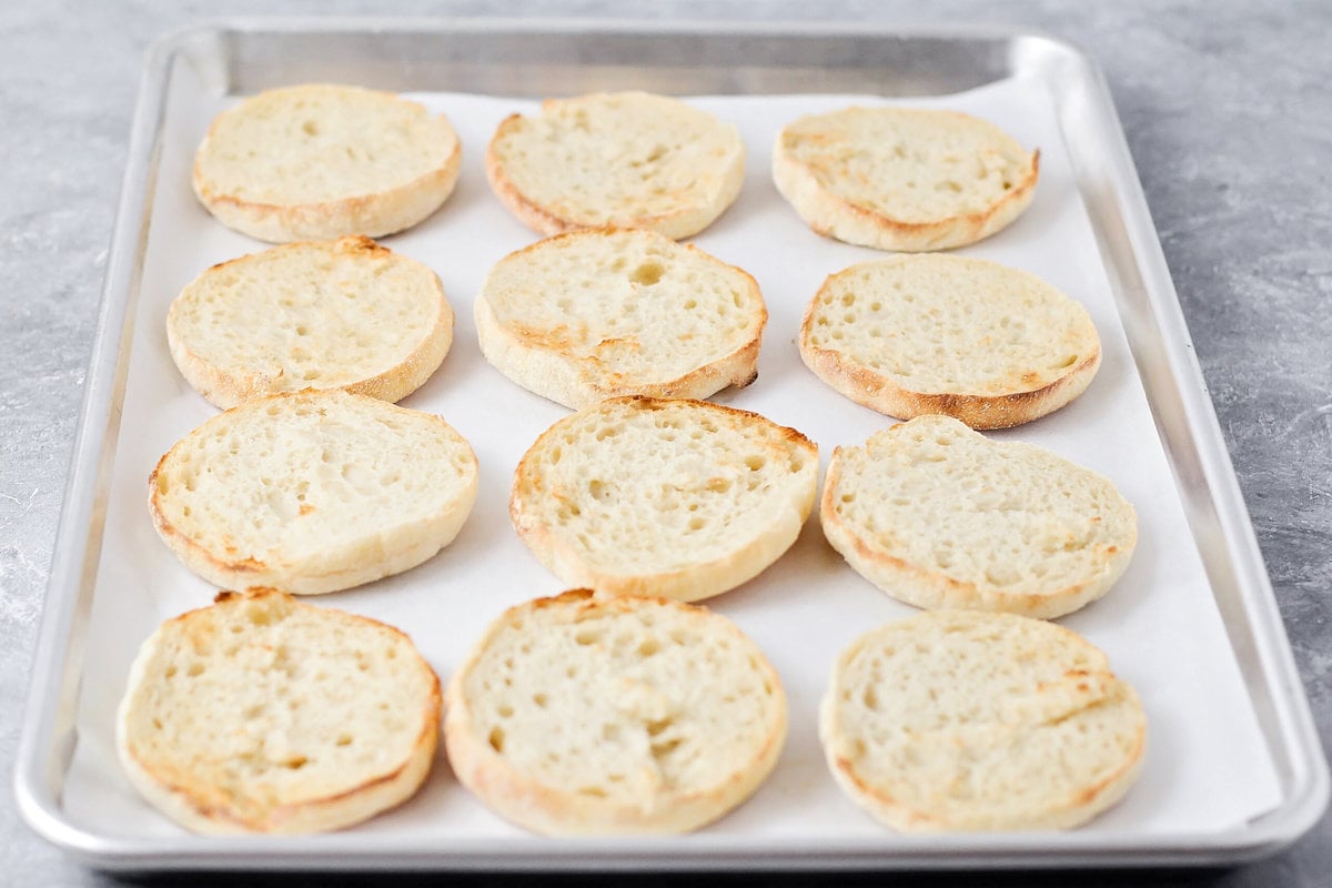 Toasted english muffins on a lined baking sheet.