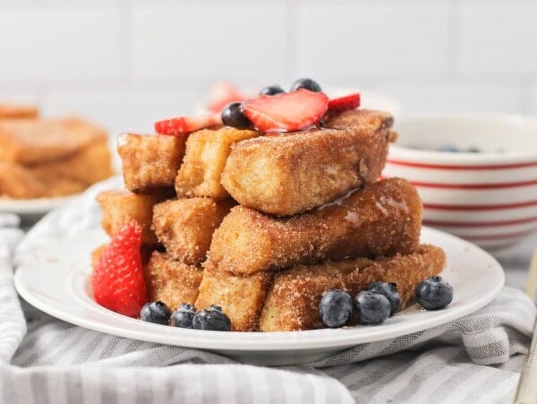 French toast sticks stacked on top of each other on a white plate.
