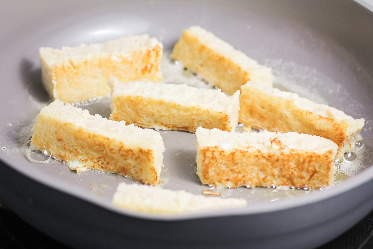 Cooked French toast sticks cooking in skillet with butter.
