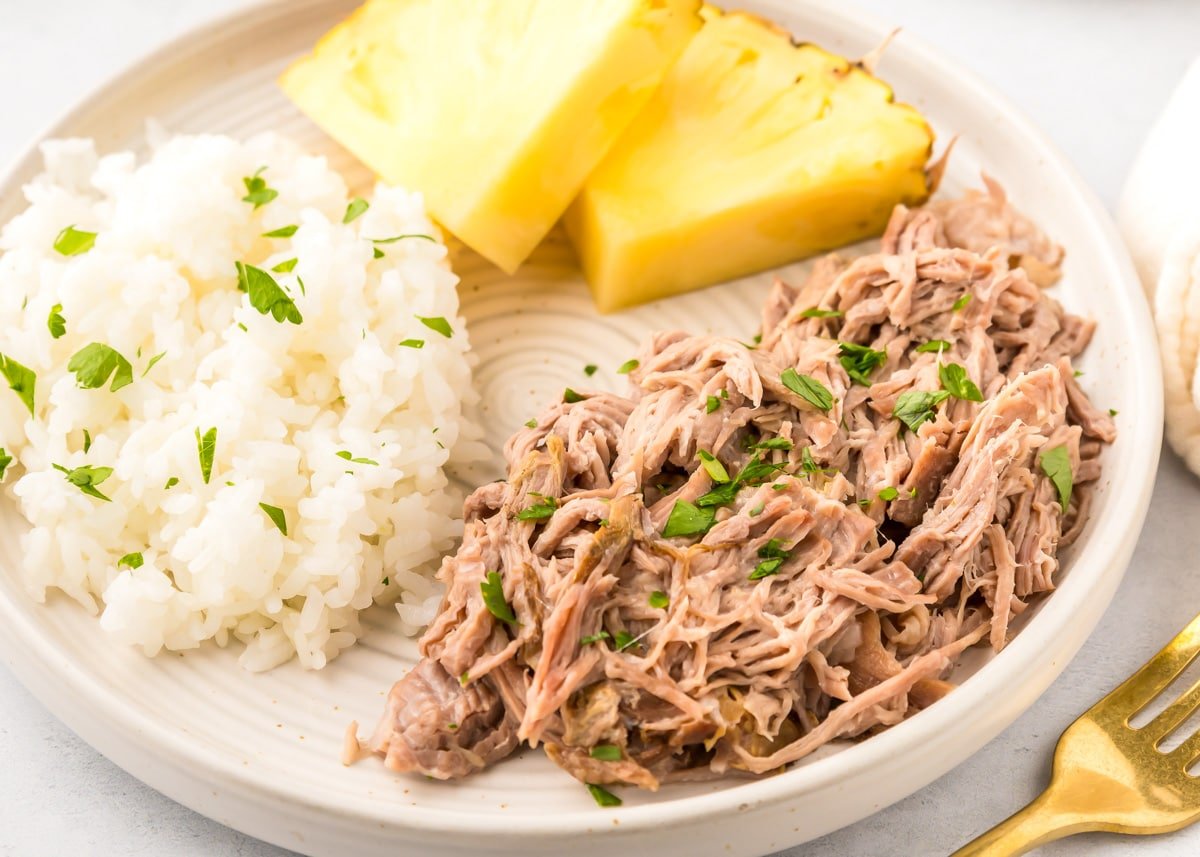 Kalua pork recipe served alongside rice and pineapple slices.