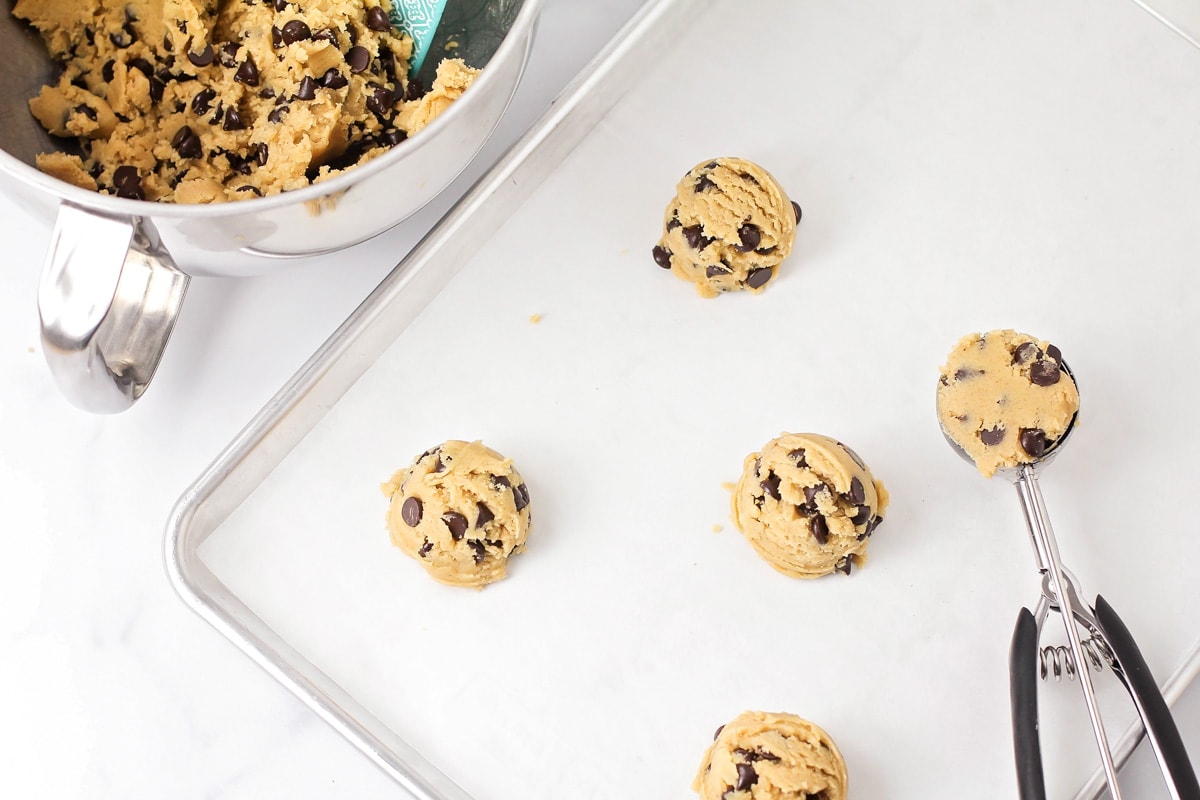 Scooping cookie dough balls onto a lined baking sheet.