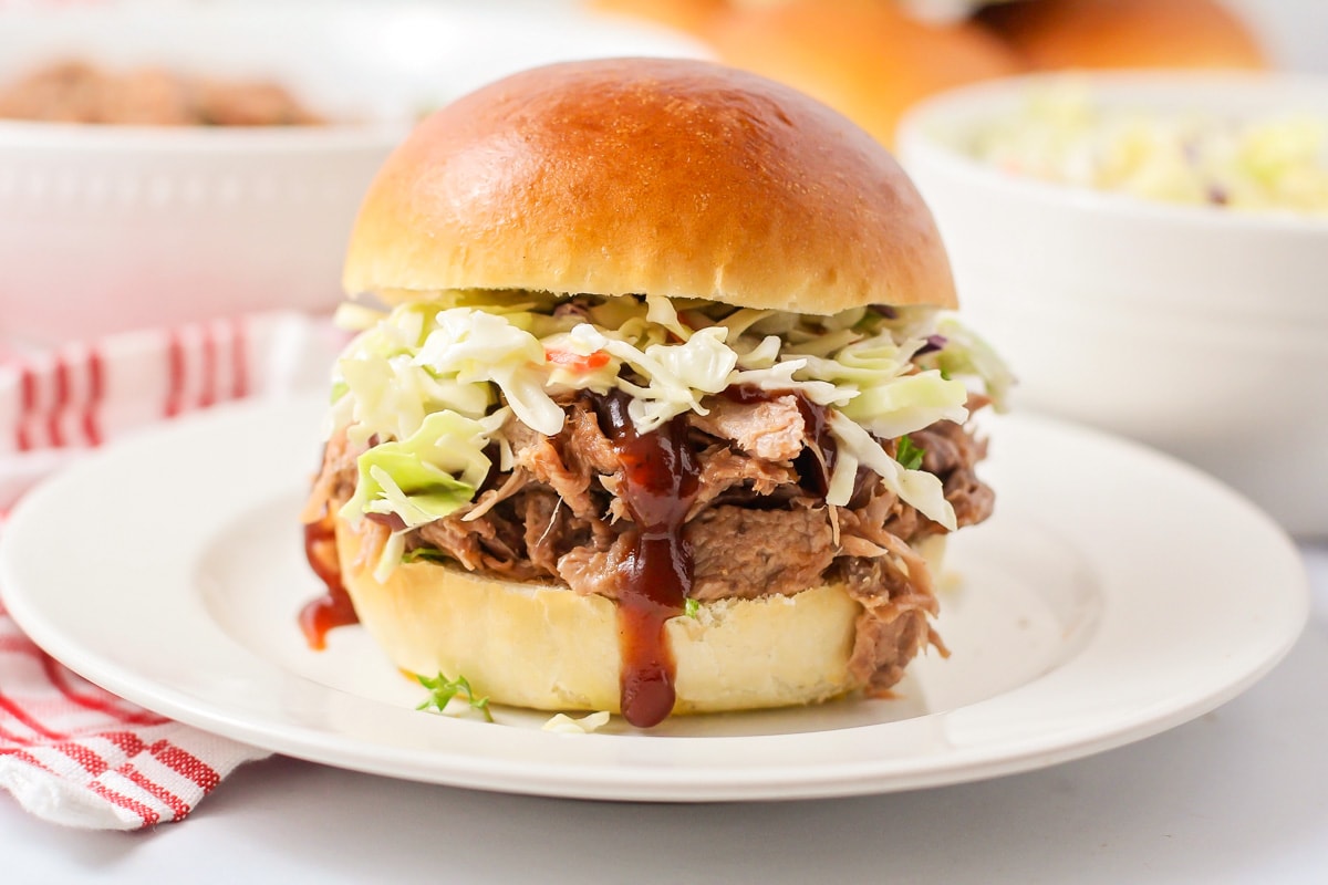 Pulled pork recipe served on a bun with coleslaw and BBQ sauce.