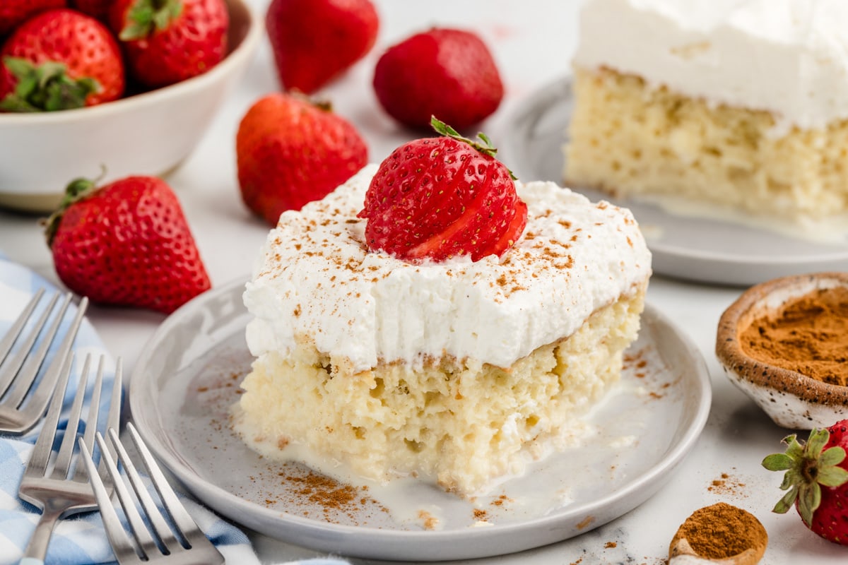 A slice of tres leches cake recipe topped with whipped cream and a strawberry.