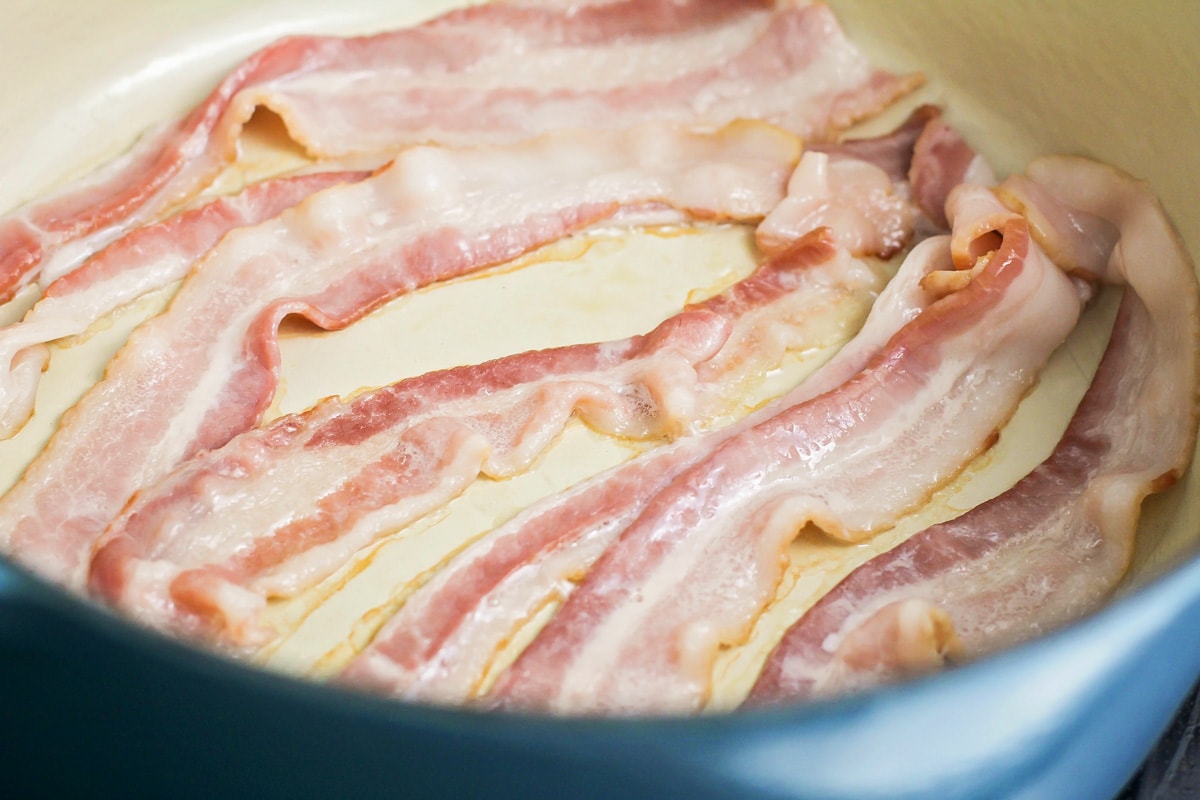 Bacon cooking in a dutch oven on a stove.