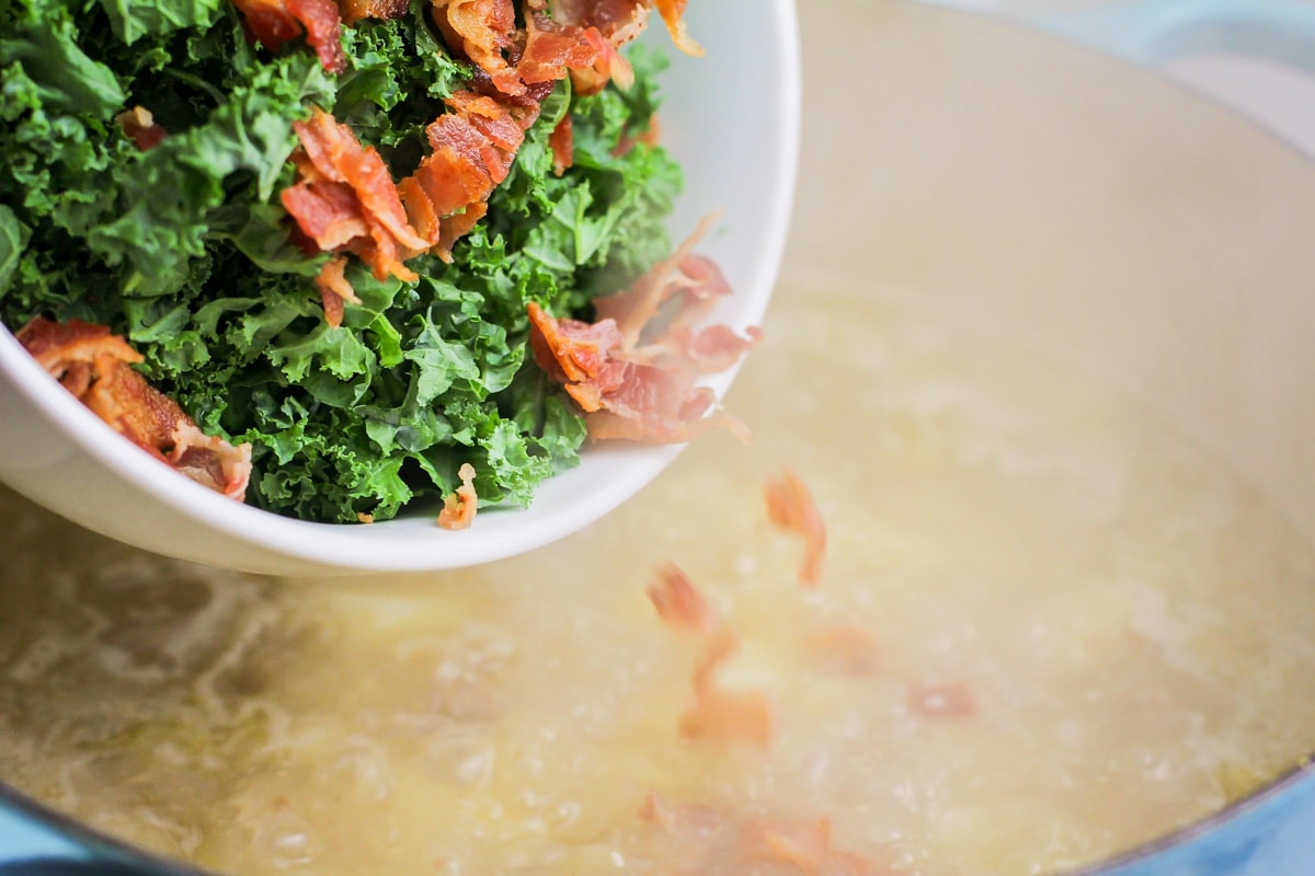Adding kale and bacon to a dutch oven of soup.