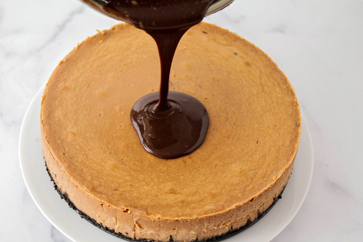 Pouring chocolate ganache on top of a baked cheesecake.