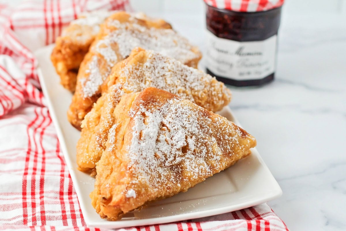 Monte cristo sandwiches on white platter with powdered sugar sprinkled on top.