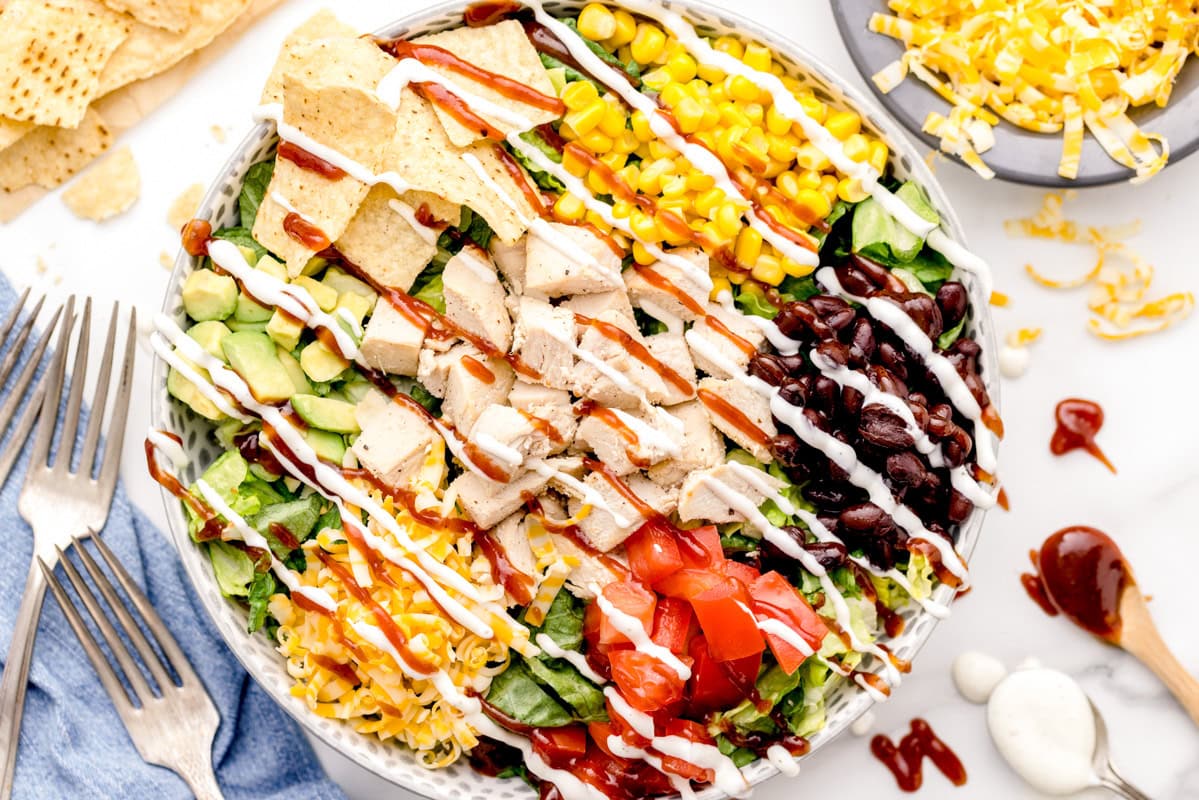 BBQ Chicken Salad recipe in a white bowl with ranch and BBQ sauce drizzled on top.