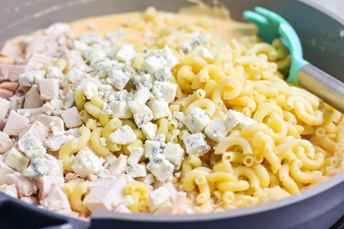 Adding pasta, cheese, and chicken to a sauce in a pan.