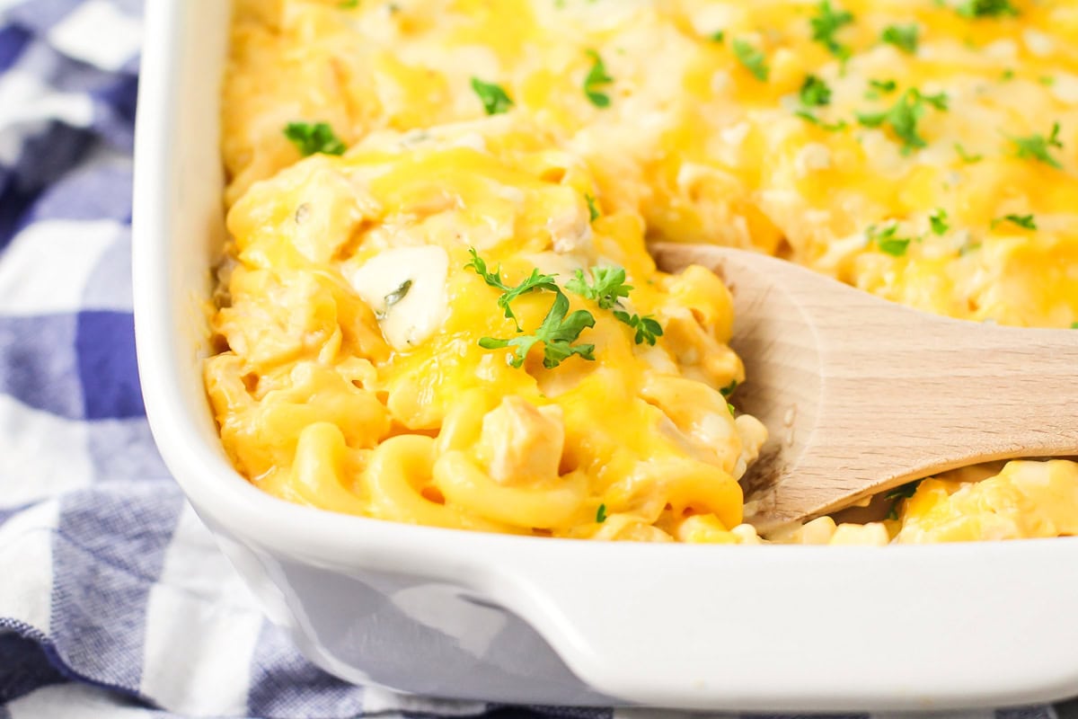 A close up of a wooden spoon scooping buffalo chicken mac and cheese from a baking dish.