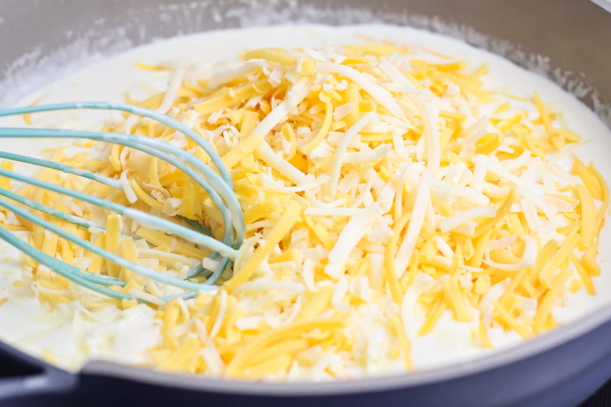 Adding shredded cheese to a sauce in a pan.