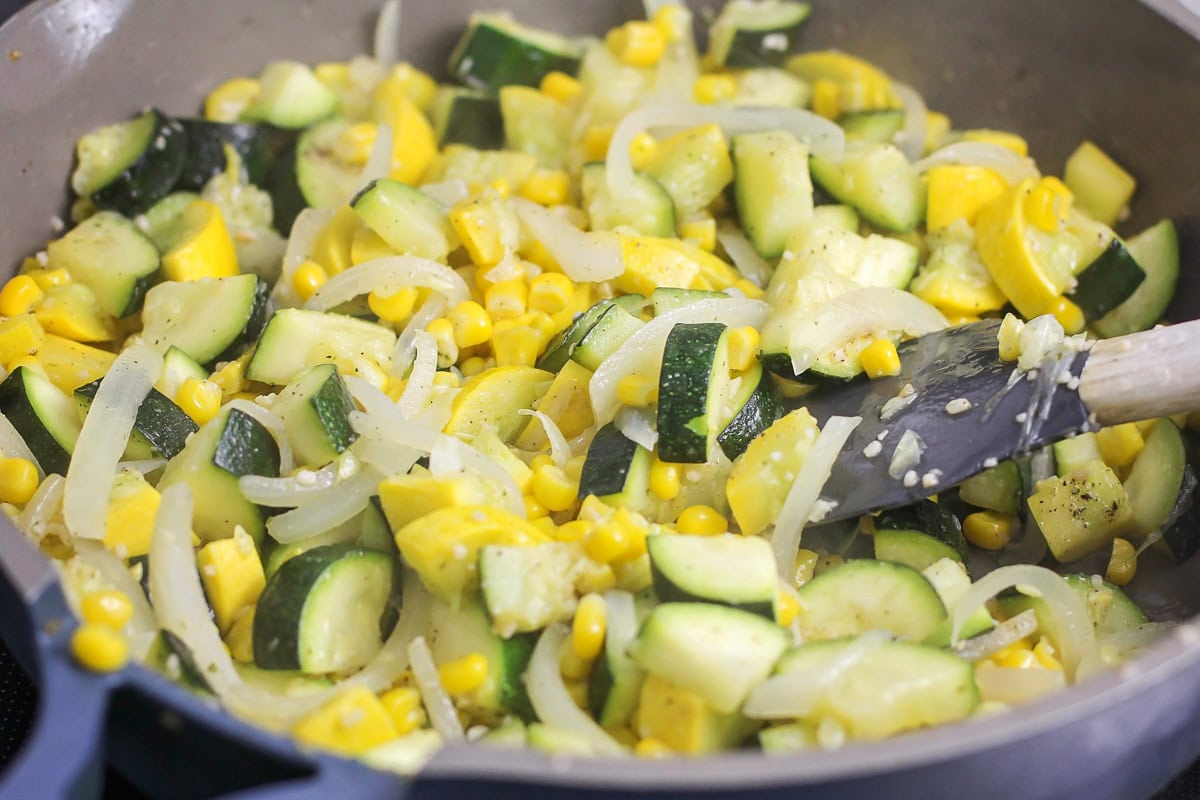 Cooking squash and veggies in a skillet on the stove.