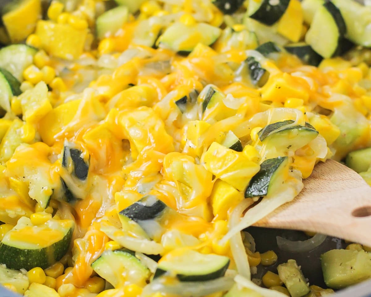 Close up of scooping cheesy calabacitas from a skillet.