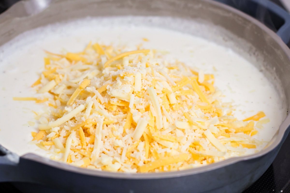 Adding shredded cheese to sauce.