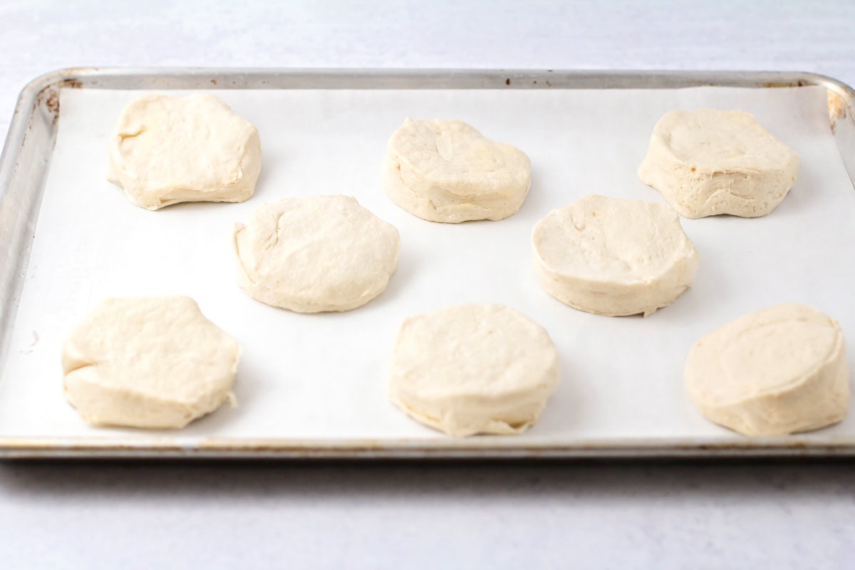 Uncooked biscuits on a lined baking sheet.