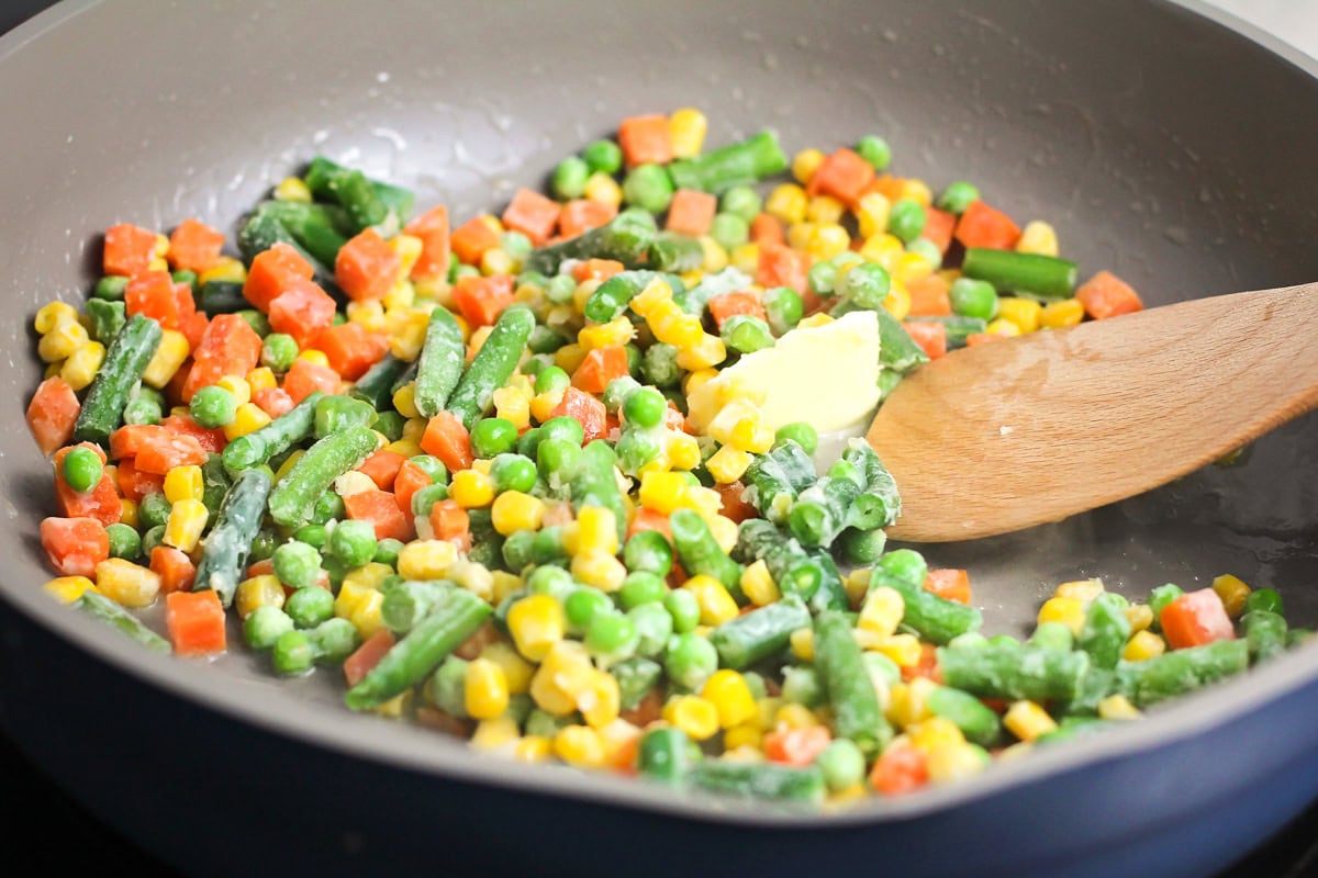 Cooking frozen mixed veggies in butter in a pan.