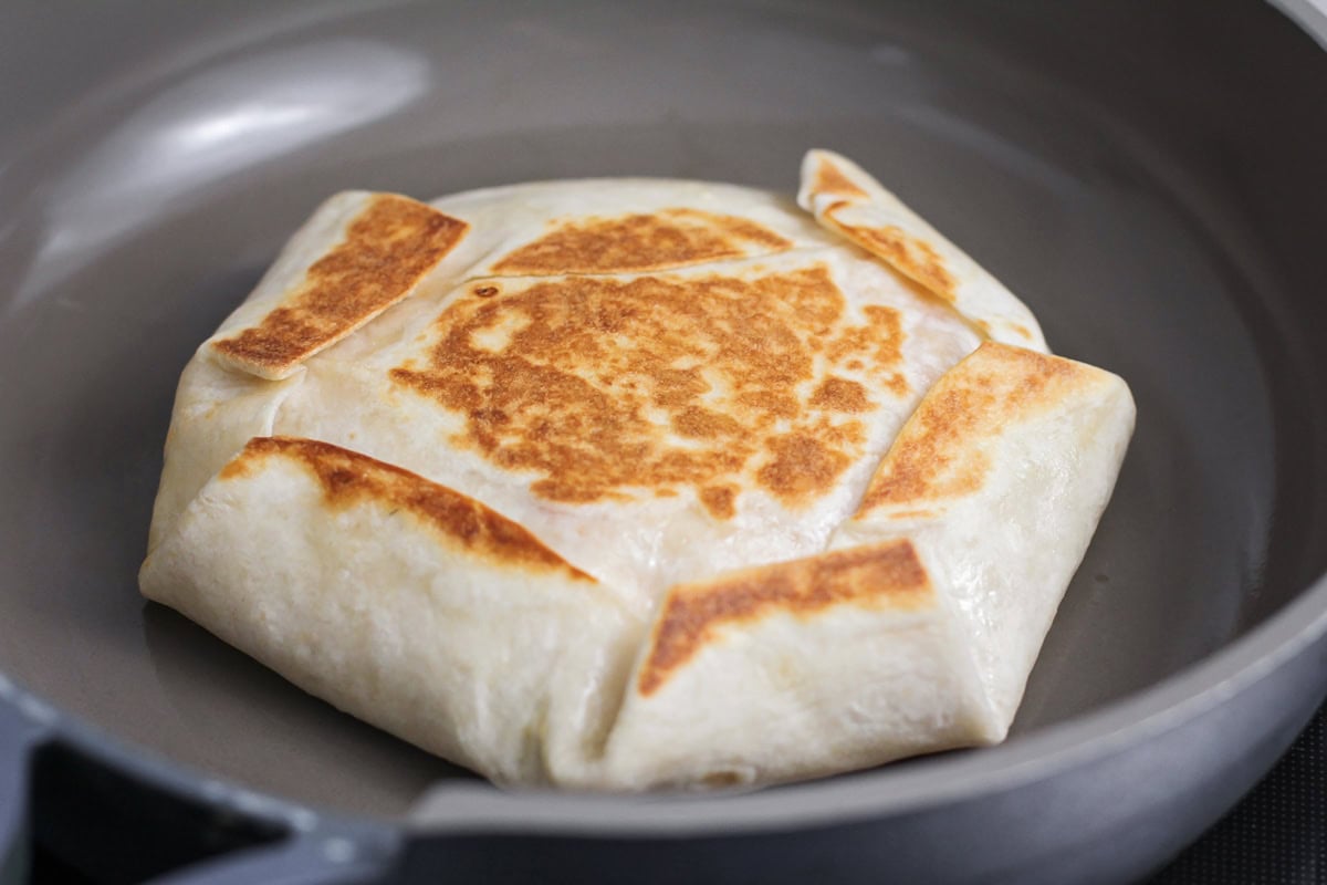 Grilling the crunchwrap in a pan on the stove.