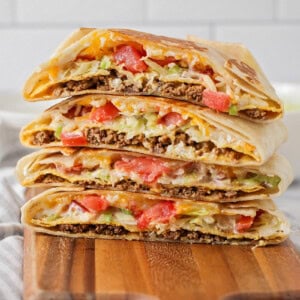 Homemade crunchwrap supremes stacked on a wooden cutting board.