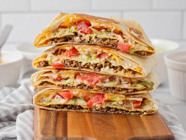 Homemade crunchwrap supremes stacked on a wooden cutting board.