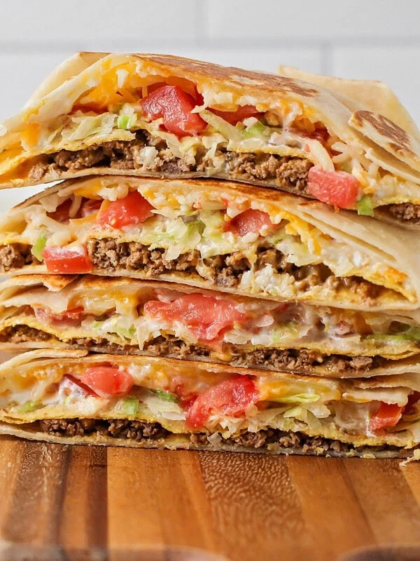 Homemade crunchwrap supremes stacked on a wooden cutting board.