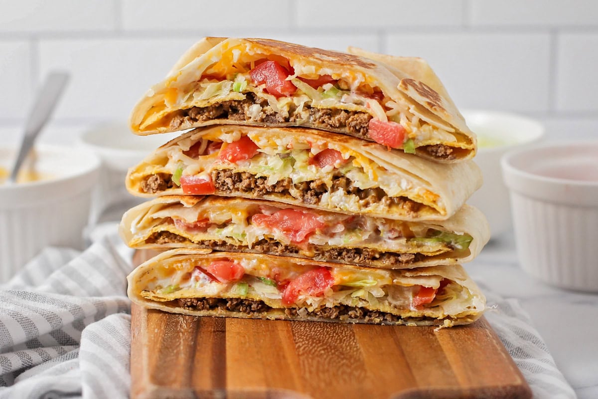 Four halved crunchwrap supreme stacked on a cutting board.