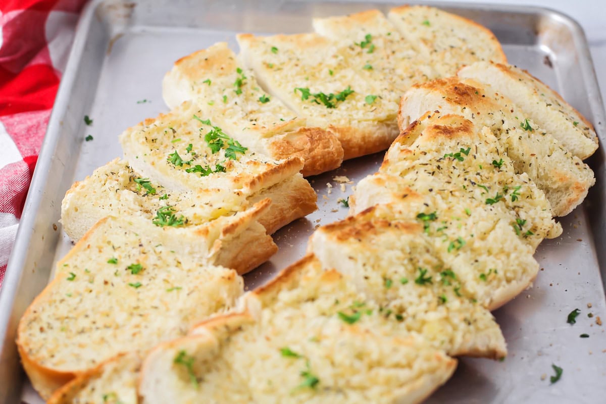 Sliced garlic bread recipe topped with fresh parsley on a baking sheet.