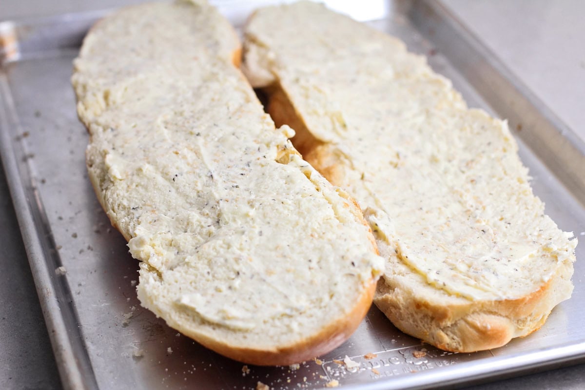 Sliced french bread topped with a butter mixture on a baking sheet.