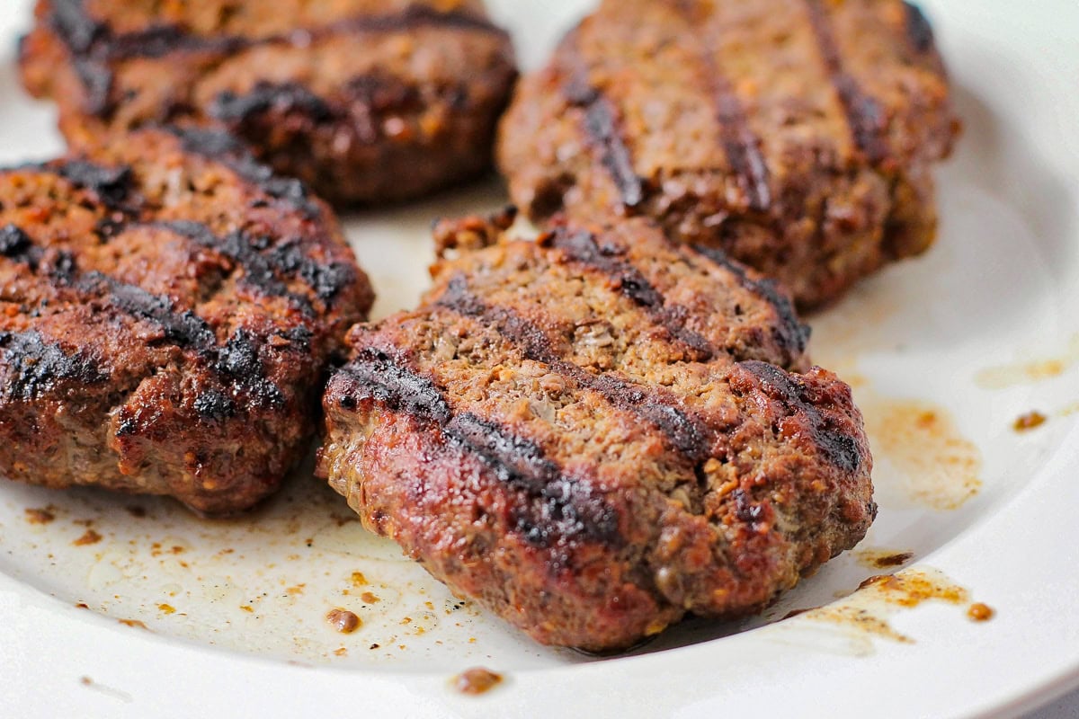 Cooked hamburgers on plate with grill marks on top.