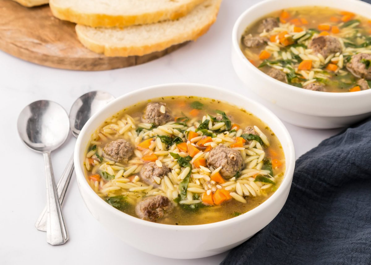 Bowls of Italian wedding soup served with fresh sliced bread.