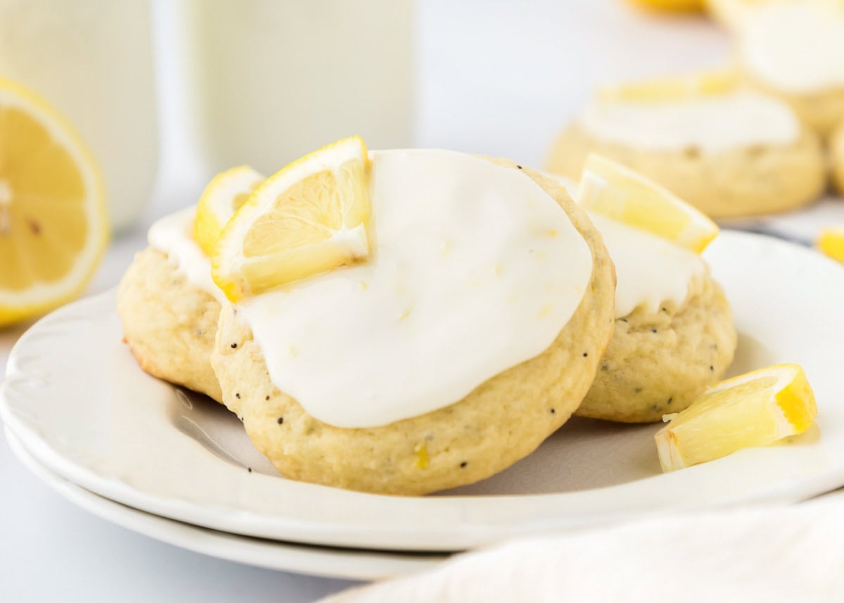 Frosted lemon poppy seed cookies topped with fresh lemon wedges on a white plate.