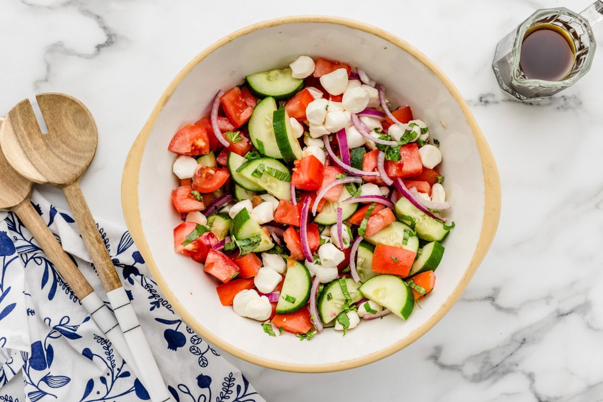 Mixing veggies and cheese with dressing in a bowl.