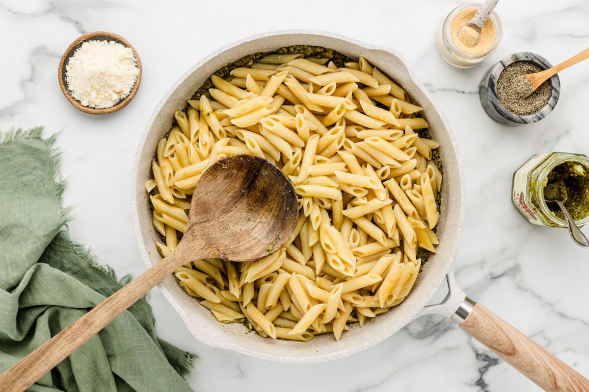 Adding cooked pasta to pesto in a pan.